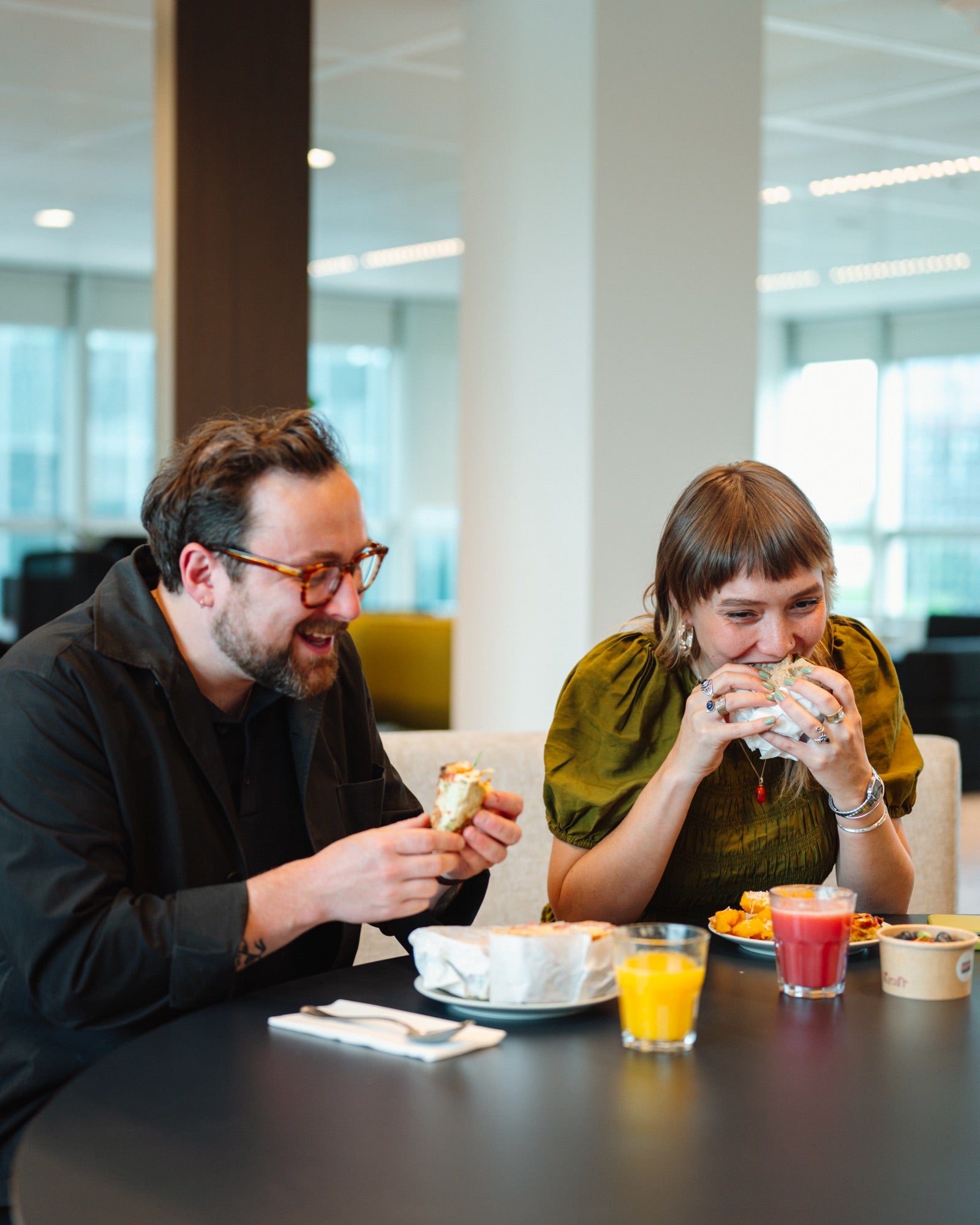 Two people sitting at a table eating and drinking in an office setting, enjoying their fresh catering delivered by Amsterdam cafe BLUEY'S