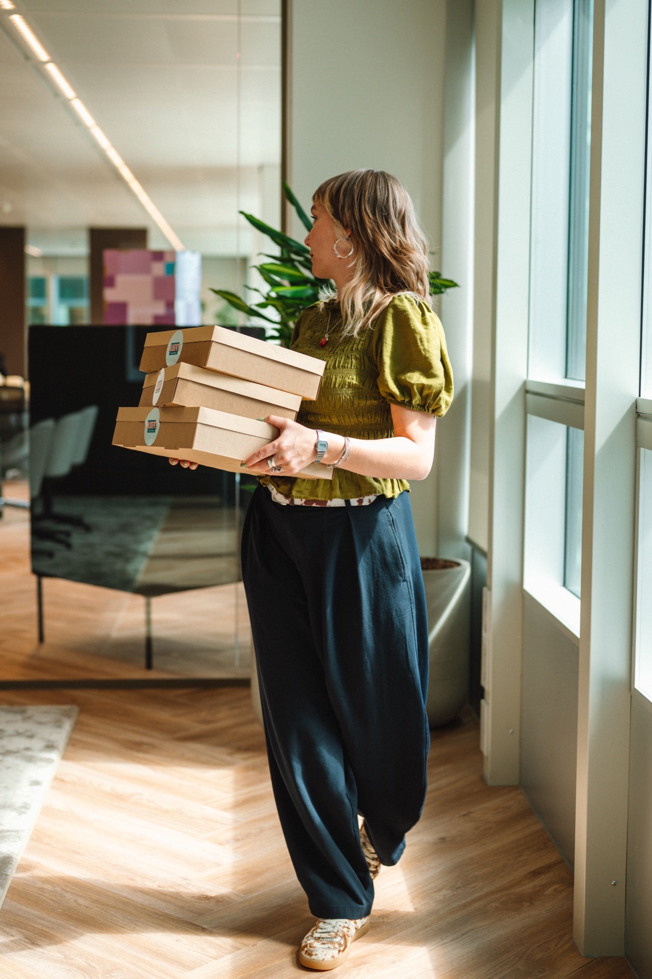Woman walking in WTC Amsterdam Zuid office holding boxes with fresh catering sandwiches.