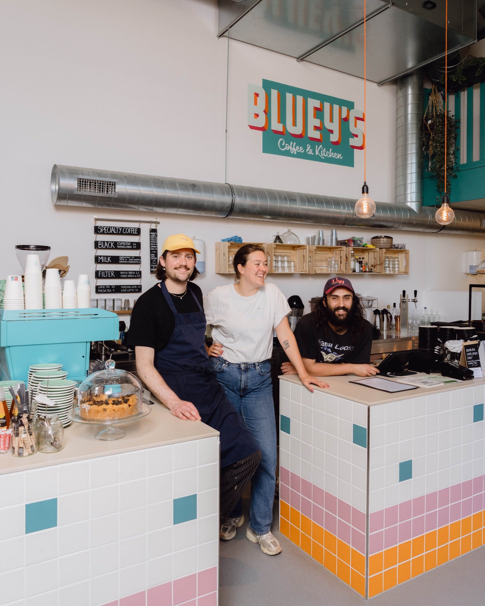 Three people standing behind a counter in a cafe named 'Bluey's Coffee & Kitchen'.