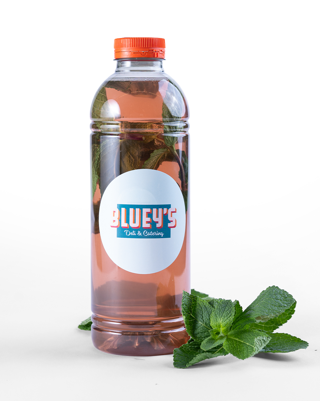 Bottle of 'Bluey's' lemonade with a orange cap and label, accompanied by mint leaves. To order with BLUEYS catering in Amsterdam.