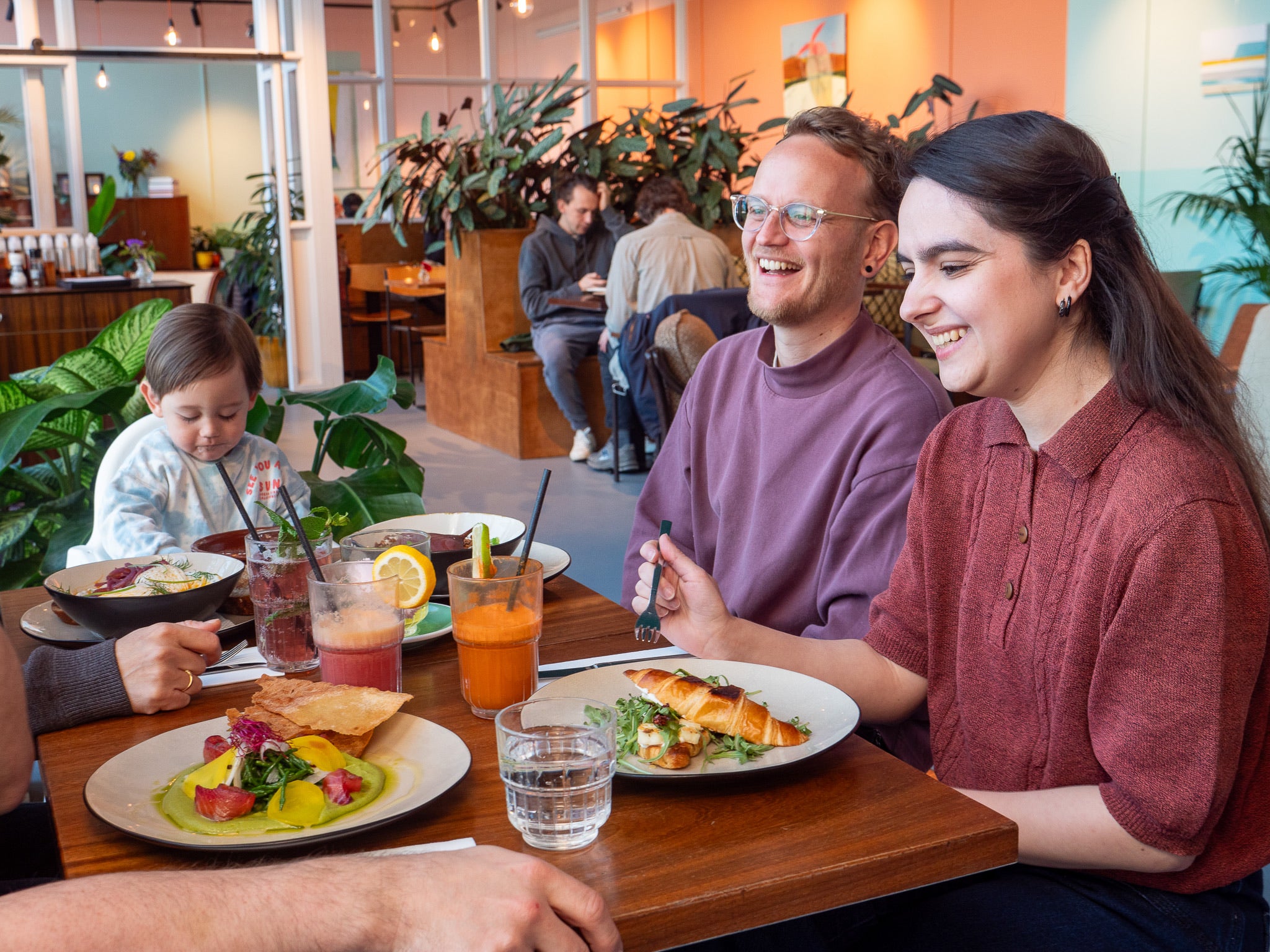 Mixed family and kid having brunch in a all-day-brunch cafè in Amsterdam Oost, surrounded by bright colours, plants, and vintage furniture