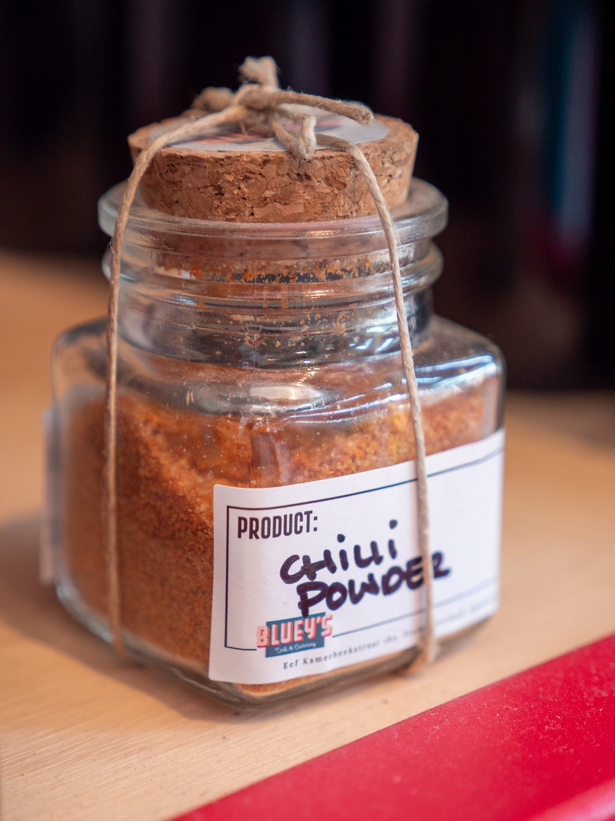 A small corked jar of Bluey's homemade chilli powder tied with twine, on the counter at the deli in Amsterdam