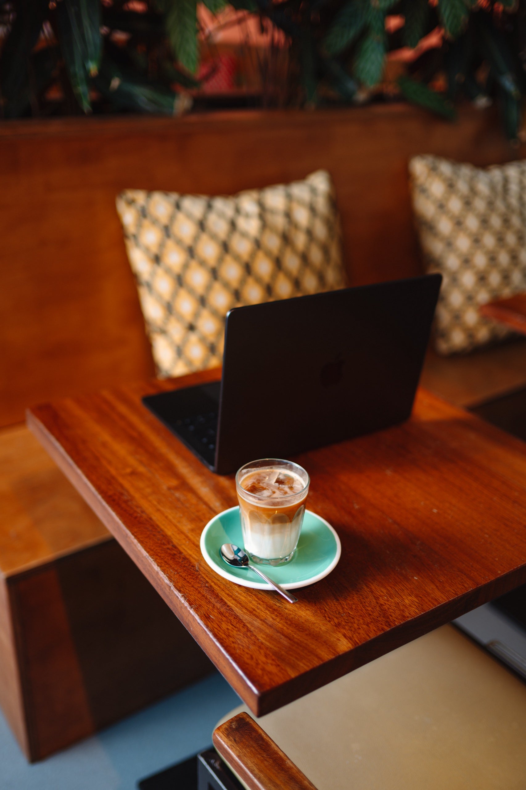 Laptop on a wooden table with a glass of iced coffee in a cozy cafe setting.